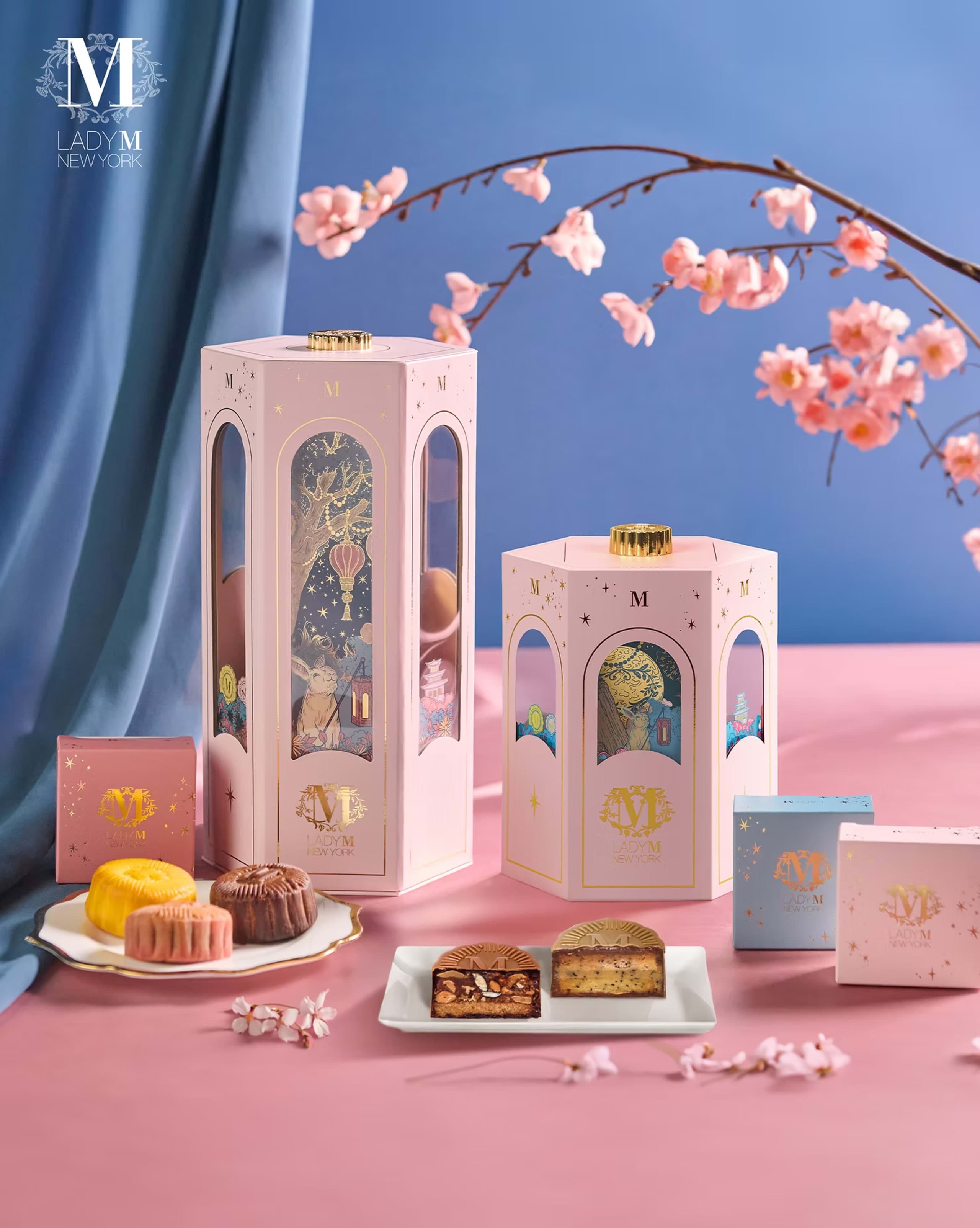 Lady M Mid-Autumn gift set: two pink hexagonal lantern boxes with gold detailing, individual boxes and mooncakes, with the jade rabbit night scene visible through the cut-out windows.